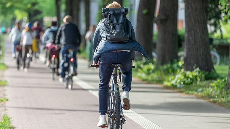 Group of people in everyday clothes cycling on a dedicated cycle path away from the camera 